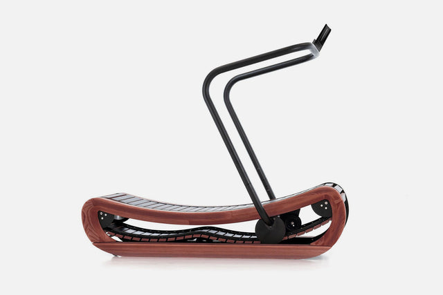 Side view of a curved manual treadmill with a dark reddish-brown wood frame, black slats, and a raised black handlebar